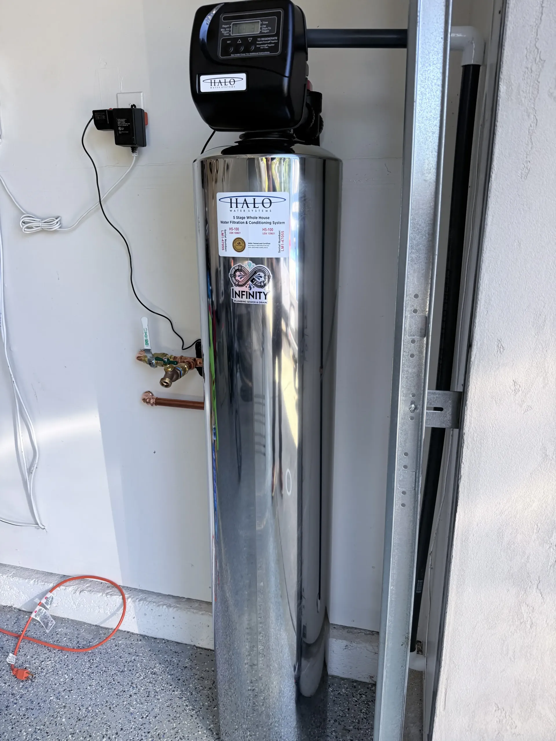 Chrome water softener tank with black control head beside a wall and garage door track