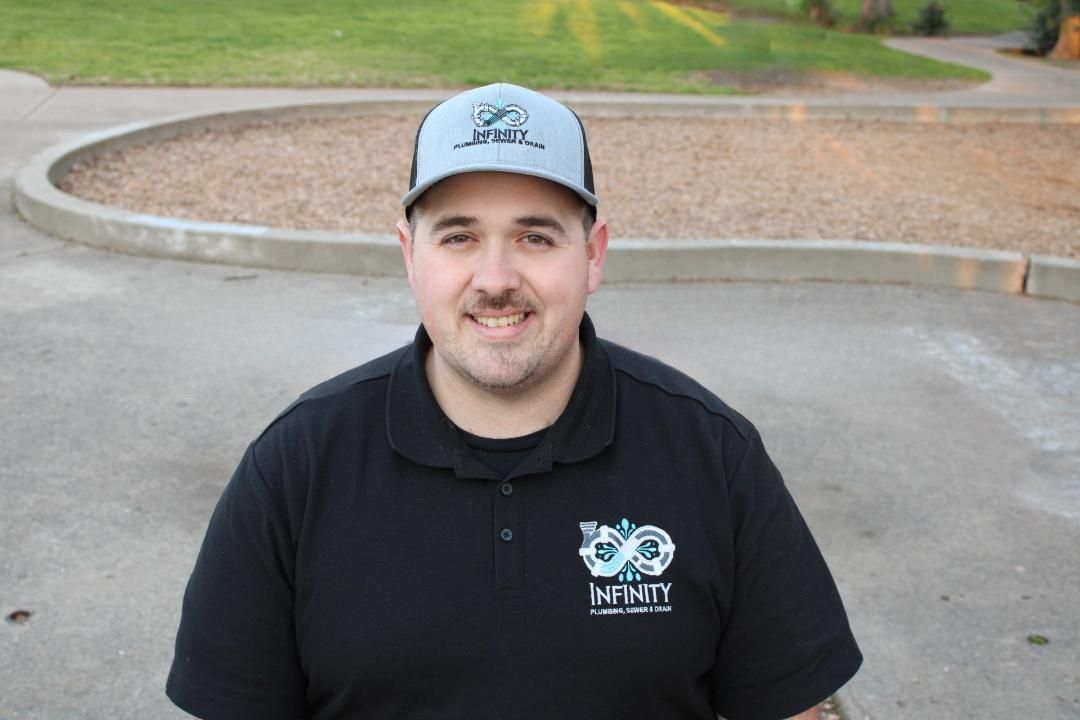 Smiling man in black polo and gray cap standing outdoors near a curb.