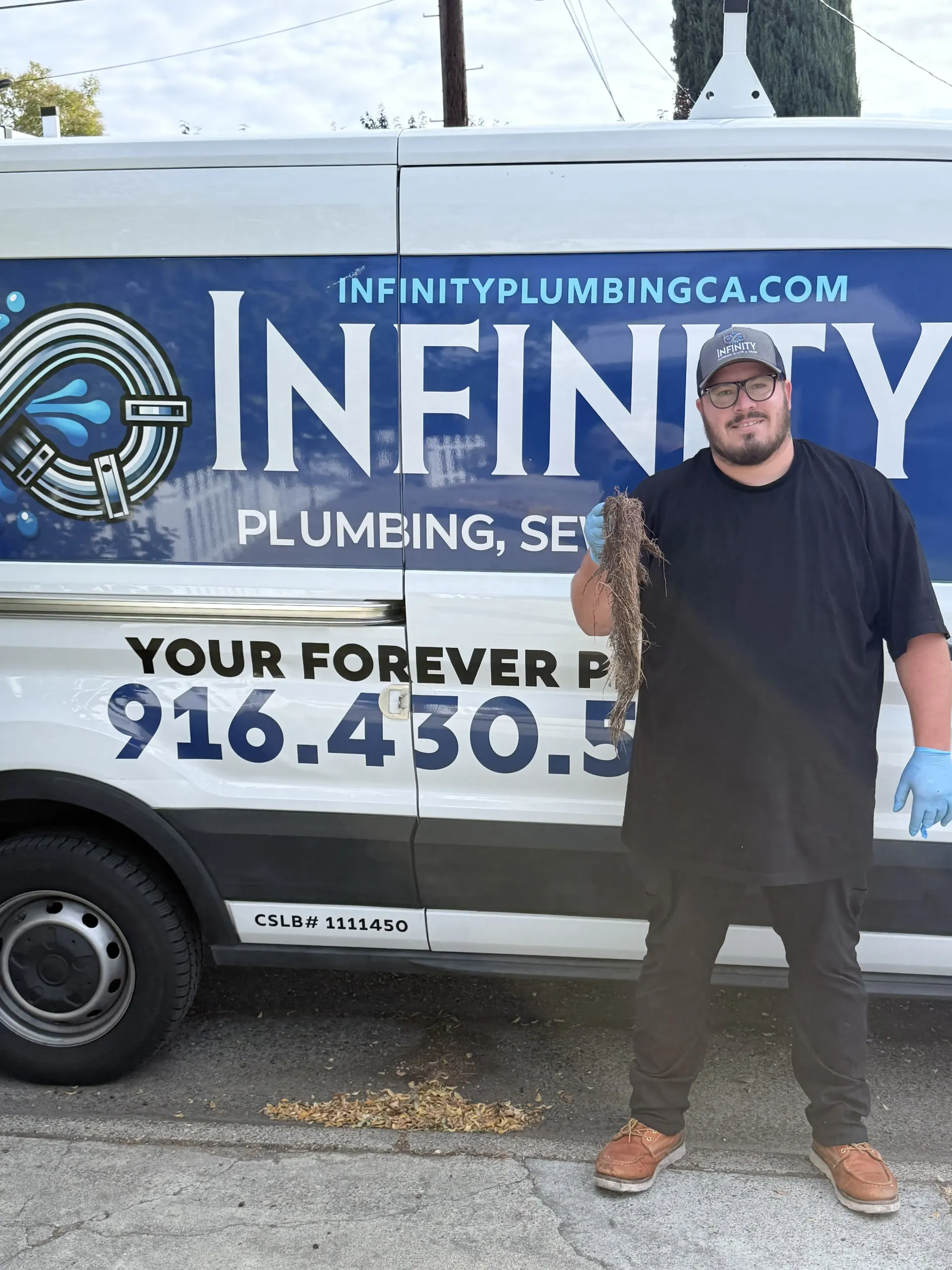 Man standing in front of a Infinity Plumbing service van with company logo and phone number visible