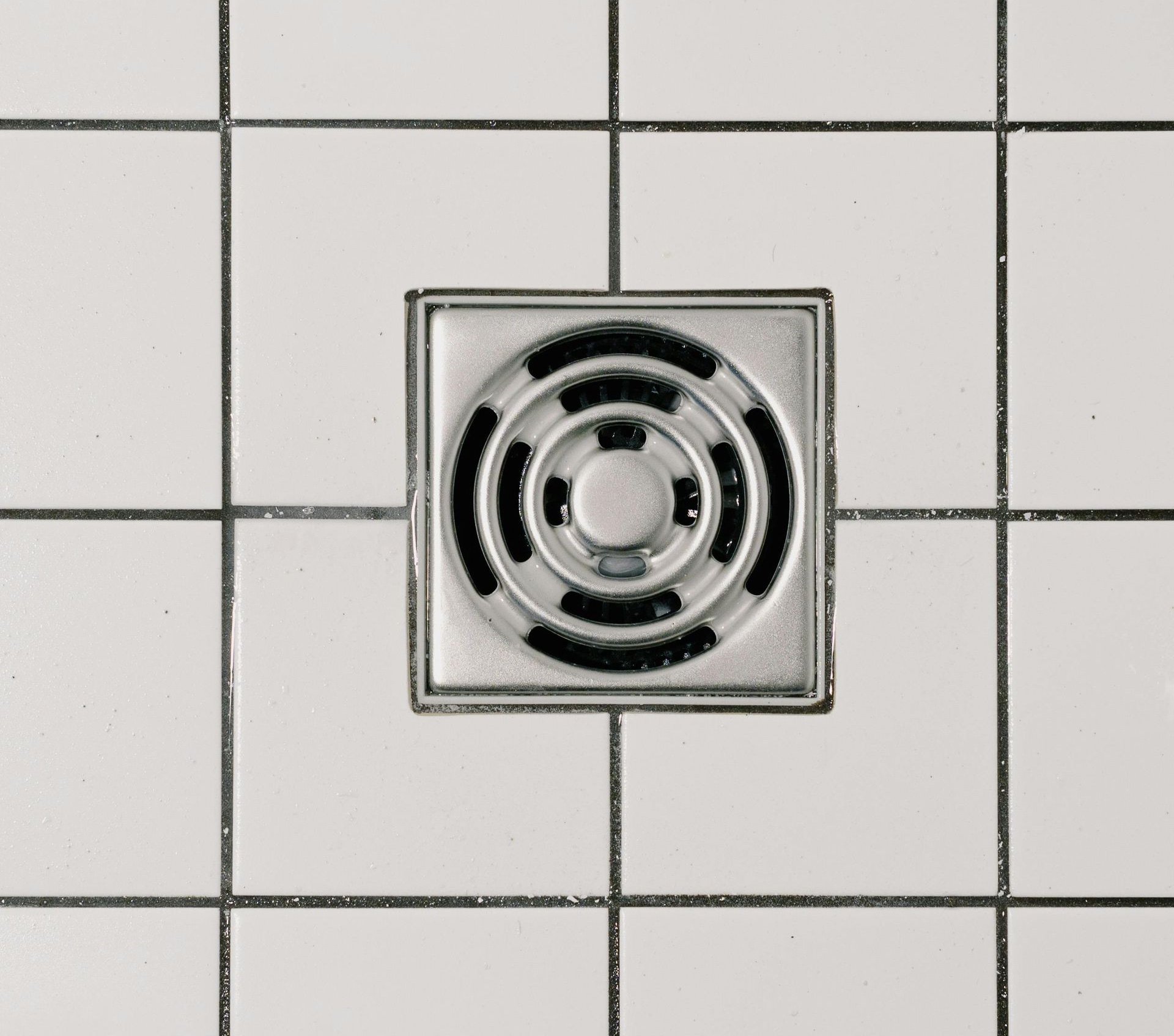 Square metal floor drain centered in white tiled surface