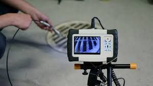 Handheld monitor on a tripod showing a blue-striped pattern, with a person’s arm reaching in from the left