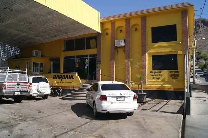Exterior de un edificio amarillo con coches blancos aparcados y una entrada cubierta.