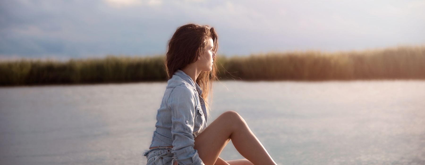 A woman is sitting on the shore of a lake with her legs crossed.