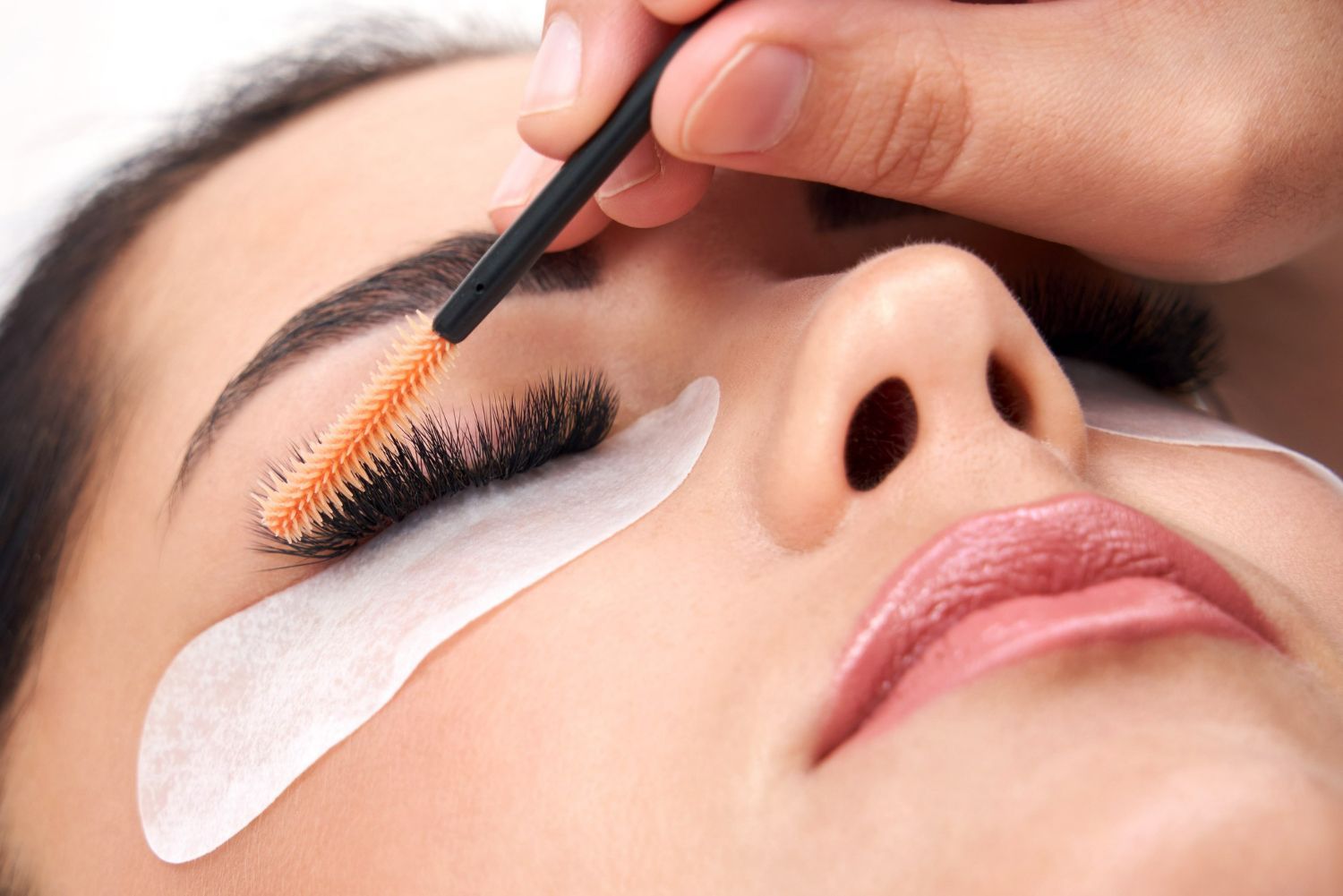 Close-up of eyelash extension application with tweezers and white under-eye pads