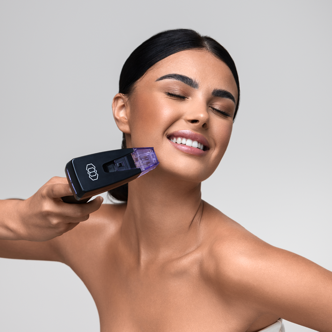 Woman smiling, using a skin treatment device on her face. Device is black, purple.