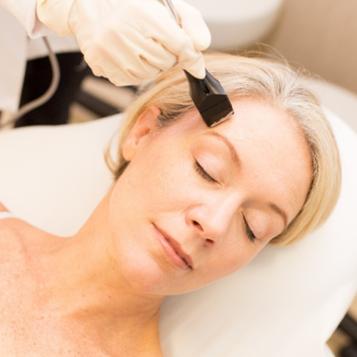 Woman receiving facial treatment with gloved hand applying product to forehead.