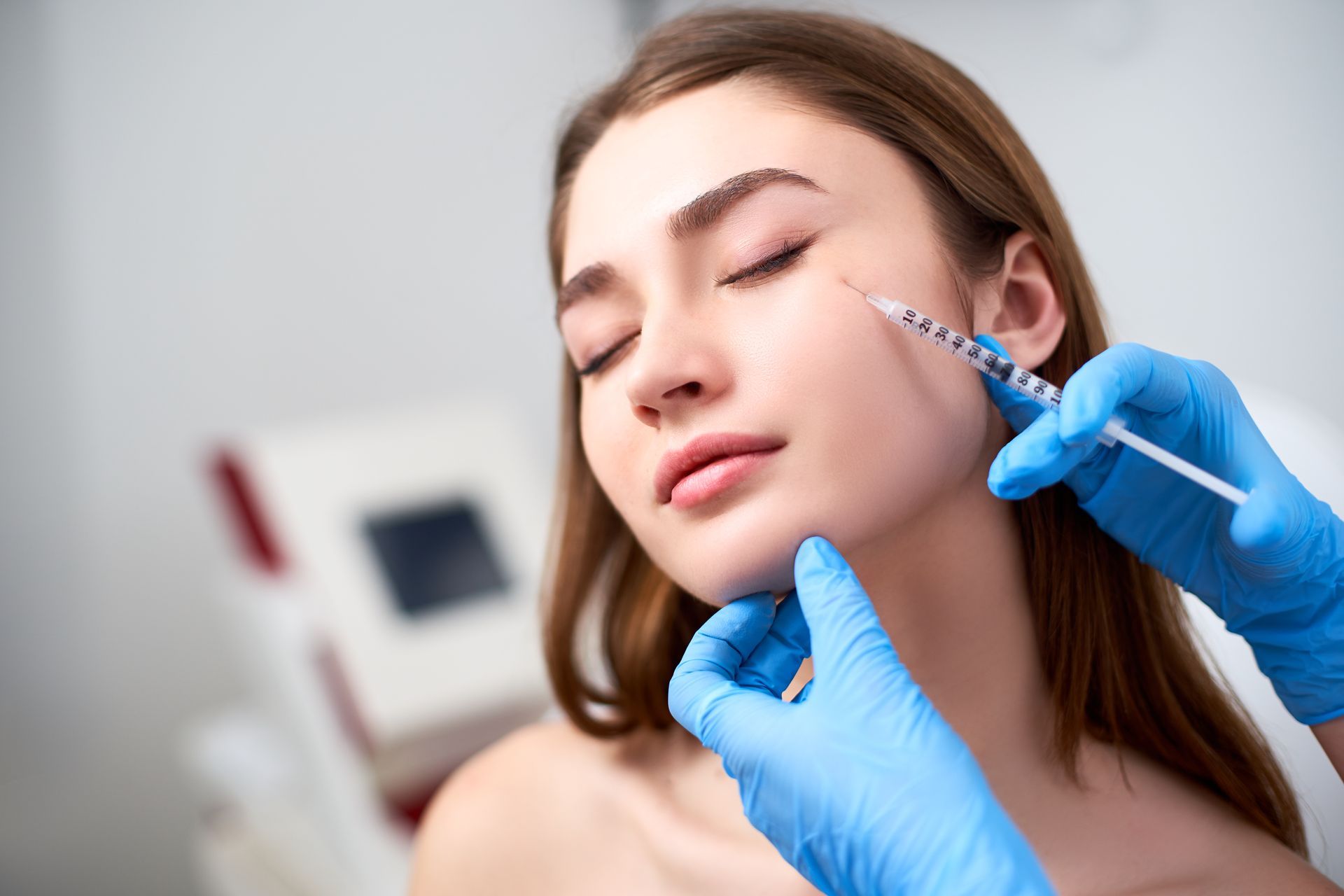 Gloved hands inject filler into a woman’s cheek in a clinic setting