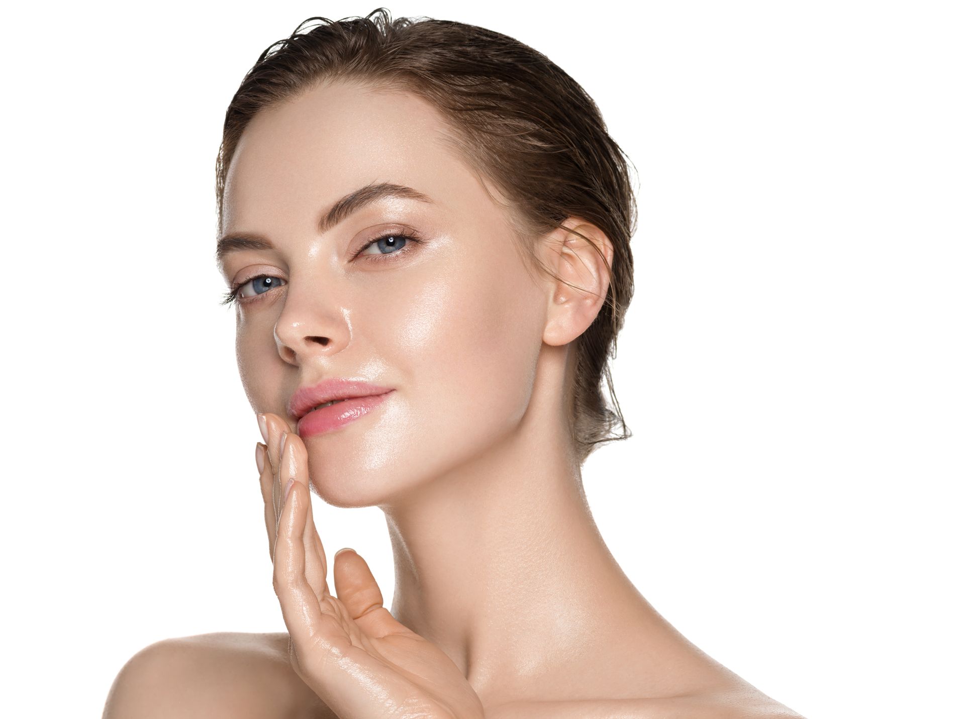 Woman with damp hair touching her face, appearing to apply skincare, close-up with a white background.