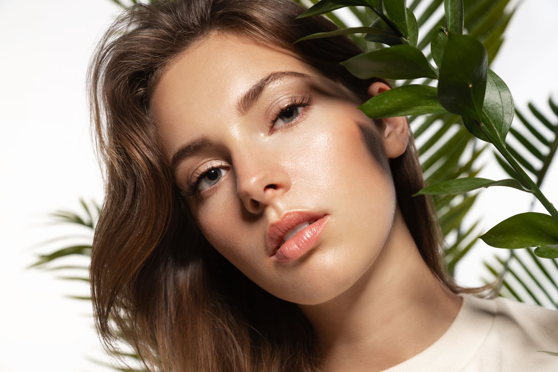 Woman with light skin, looking at the camera, framed by green leaves, against a white background.