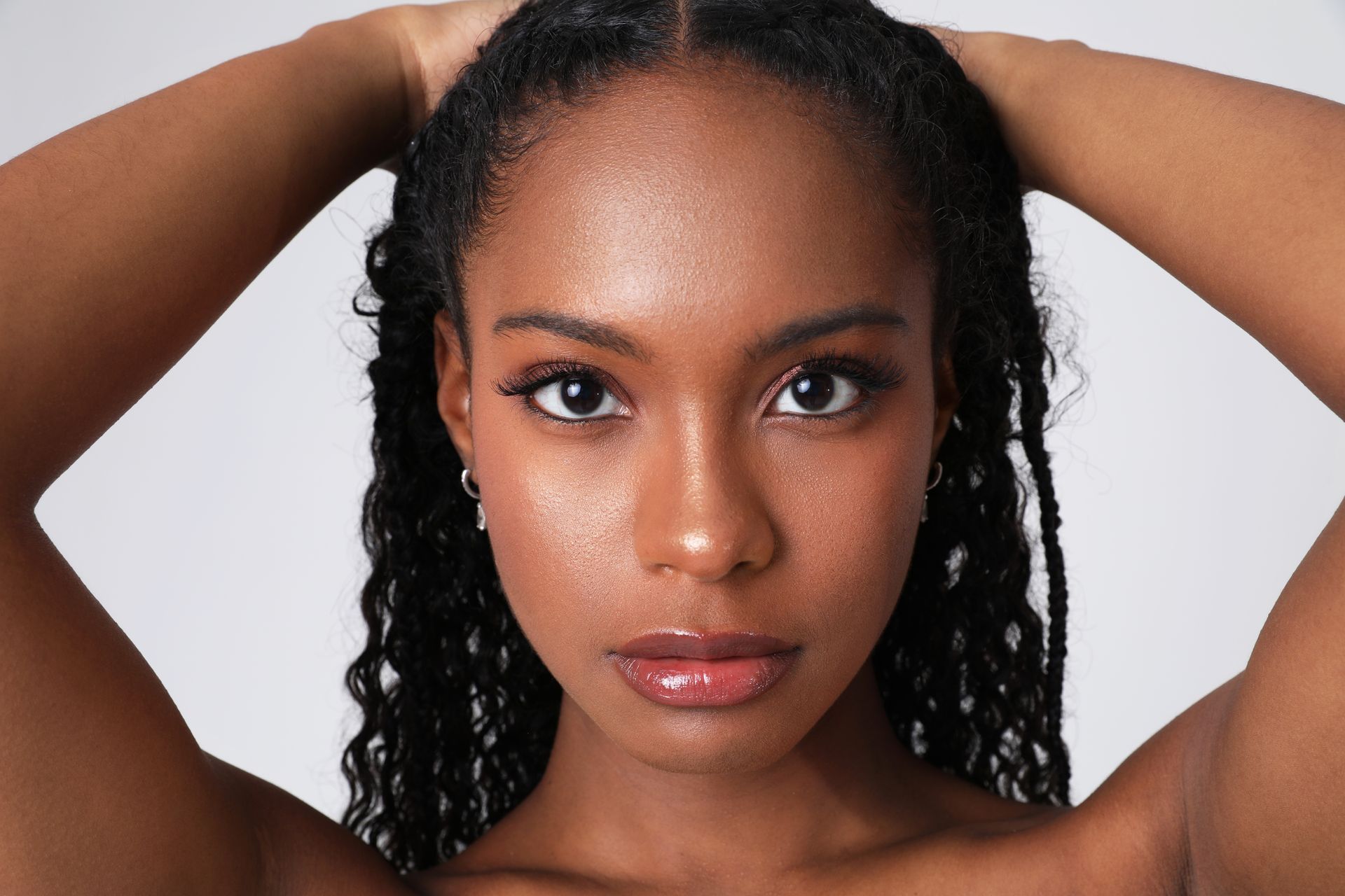 Woman with braided hair, hands behind head, looking at the viewer.