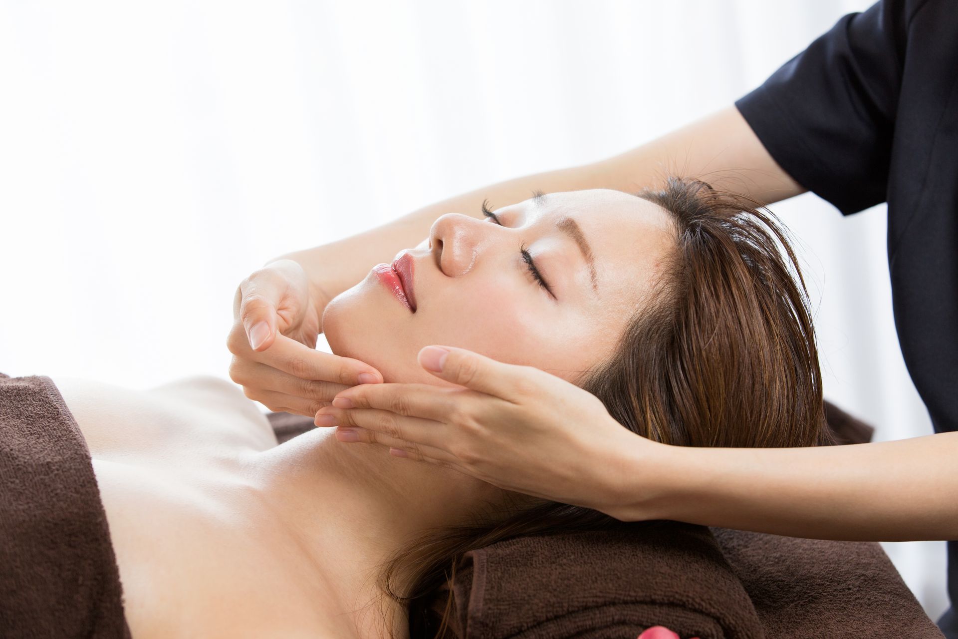 Woman receiving a facial massage at a spa; hands on her face.