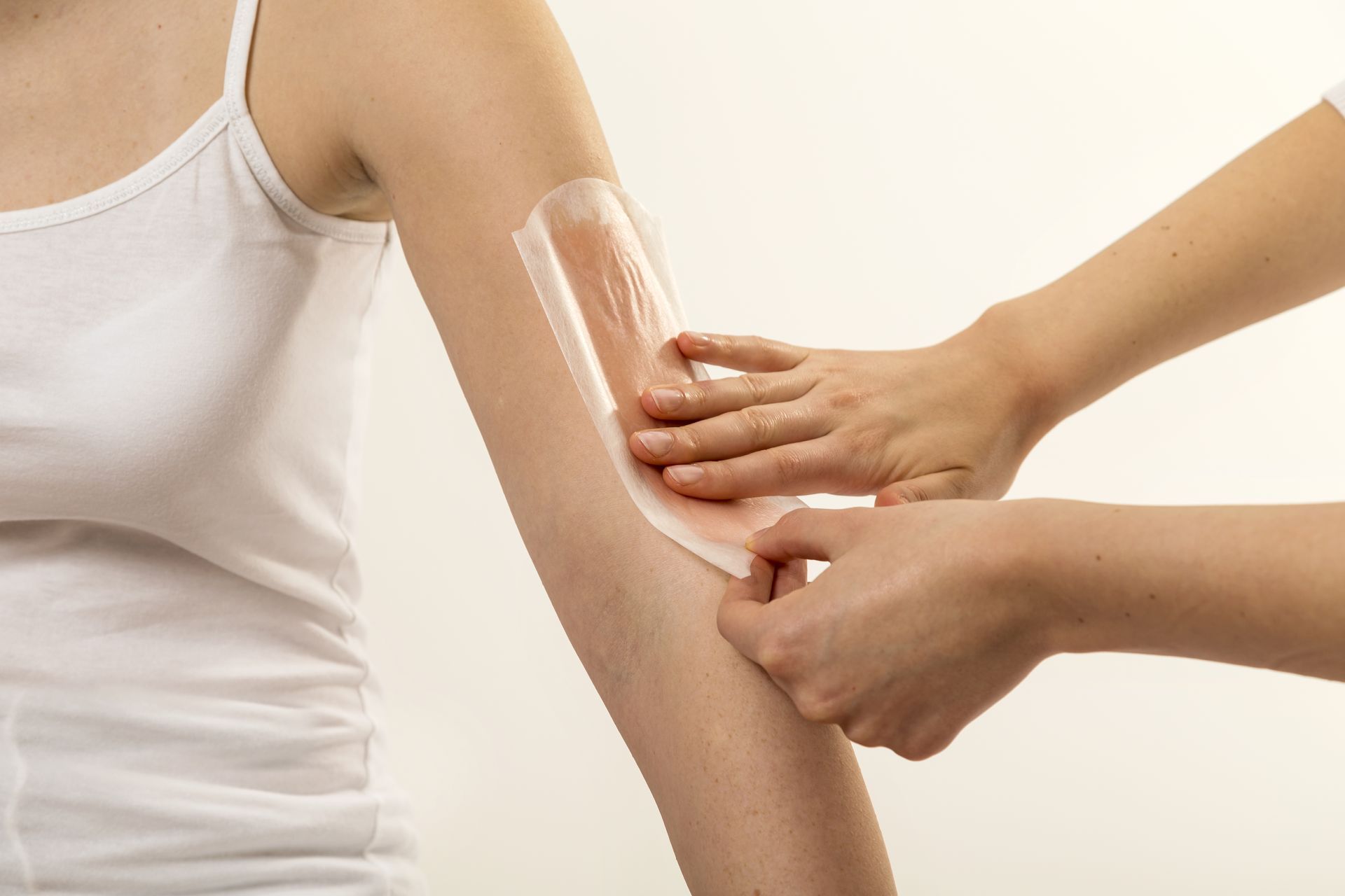 A person applying a wax strip to another individual’s arm for hair removal.