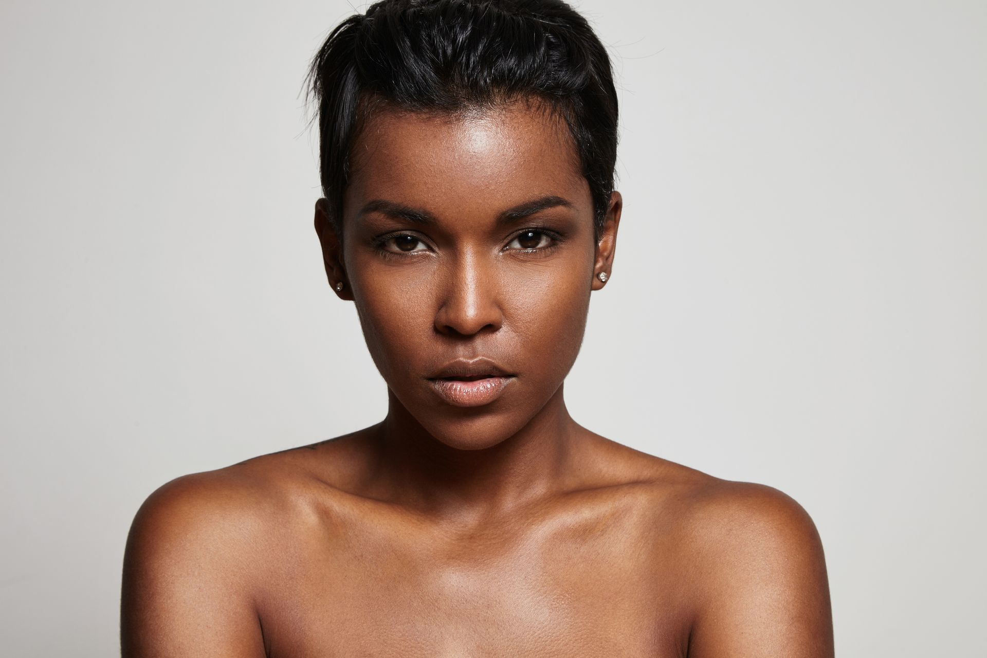 Woman with dark skin and short, dark hair, looking directly at the viewer with a neutral expression.
