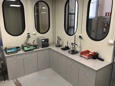 Ambiente di lavoro pulito in laboratorio, con armadietti, microscopi e apparecchiature elettroniche posizionati sotto finestre interne ovali.