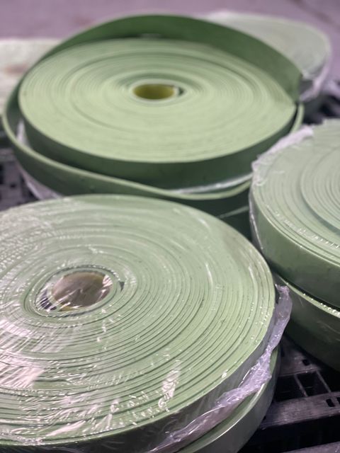 Pile di cinghie arrotolate verde chiaro con centro metallico, disposte ordinatamente su una superficie