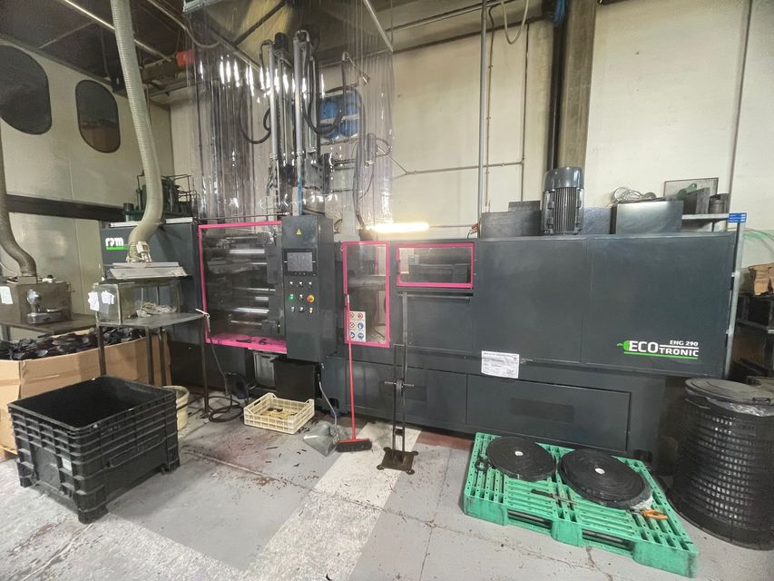 Un grosso macchinario industriale nero in un'officina, con nastro adesivo rosa e casse nere impilate nelle vicinanze.