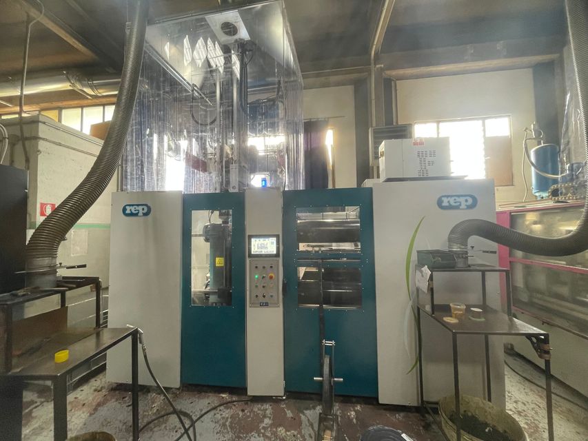 Macchinario industriale in una fabbrica, con pannelli color verde acqua e teli di plastica trasparente sopra.