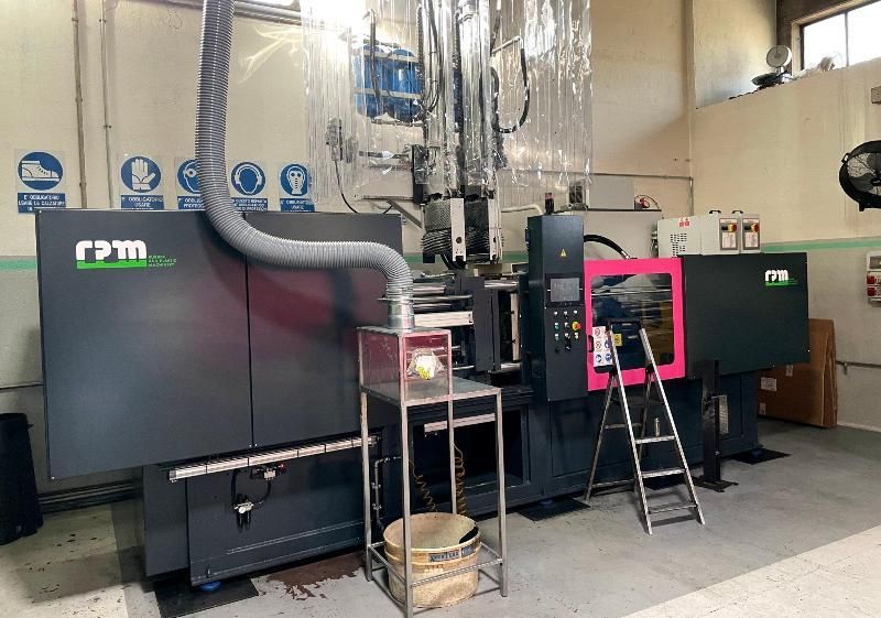 Grande macchinario industriale in un'officina, con pannello di controllo evidenziato in rosa e scala nella parte anteriore.