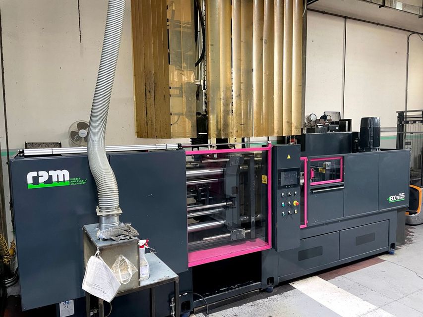 Grande macchinario industriale nero e rosa all'interno di una fabbrica, con tubi e parti metalliche a vista.