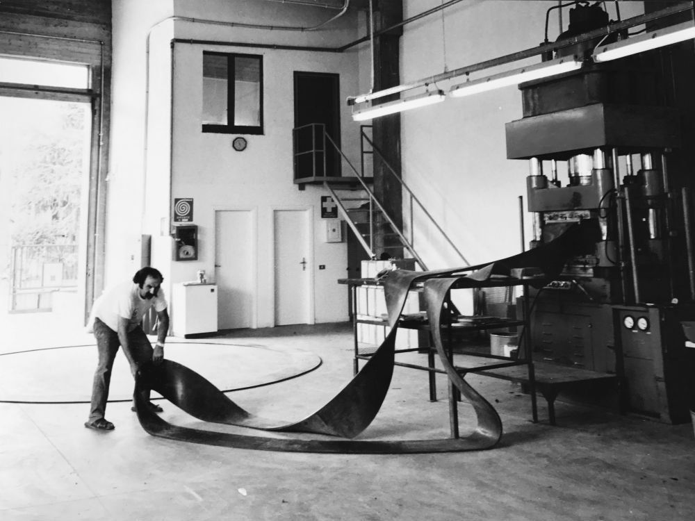 Una persona è china su un grande telo nero in un'officina industriale con scale metalliche e macchinari.