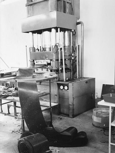 Officina industriale con una grande pressa idraulica e pezzi sparsi sul pavimento.