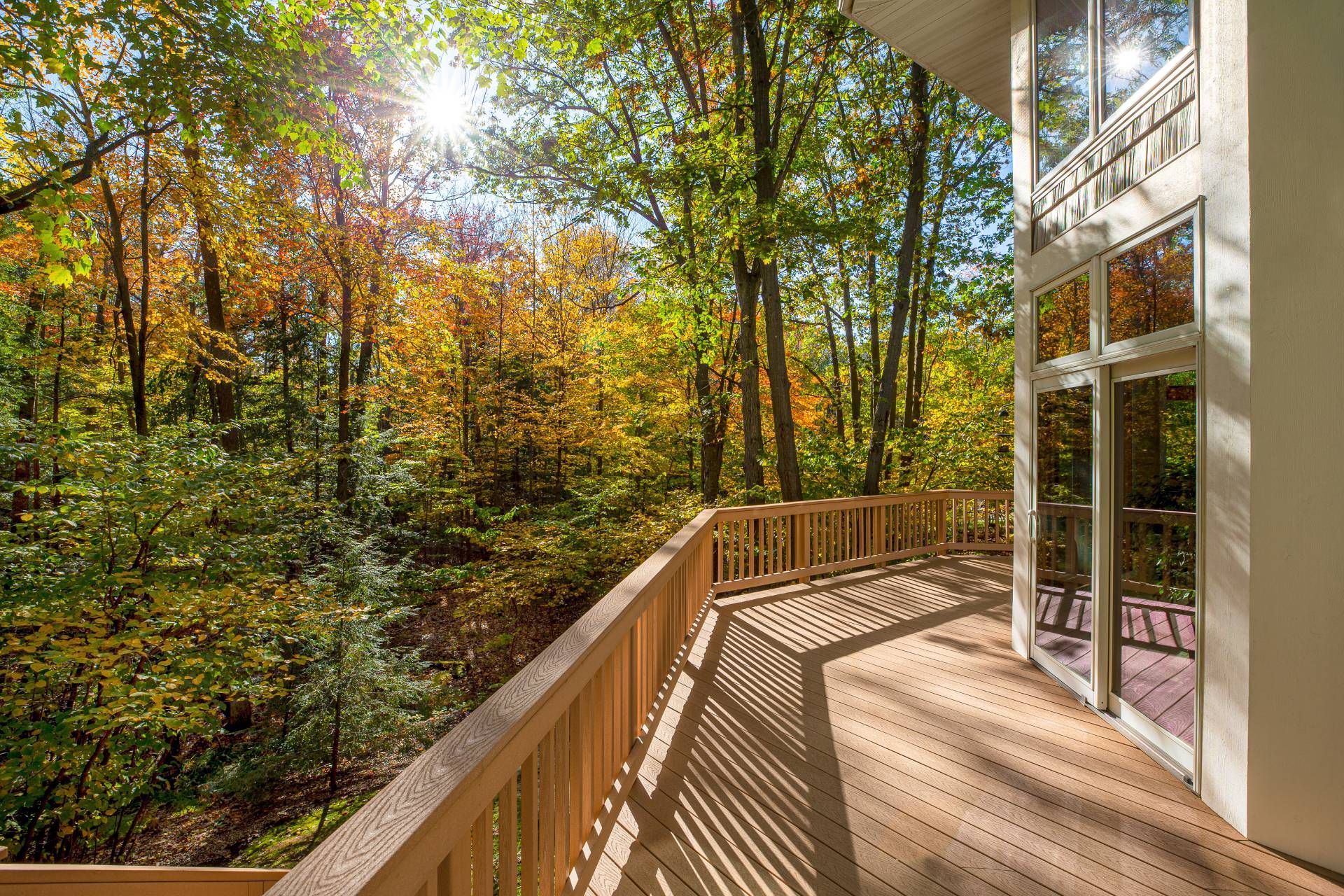 A gorgeous, large composite deck surrounding a home with trees in fall hues nearby