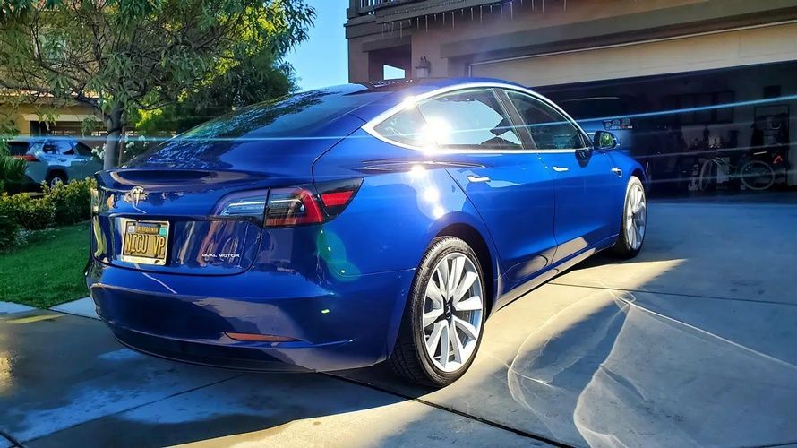 A blue tesla model 3 is parked in a driveway in front of a house.