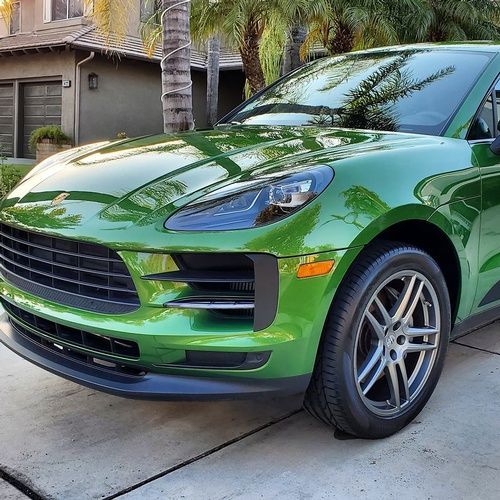 A green porsche macan is parked in a driveway in front of a house.