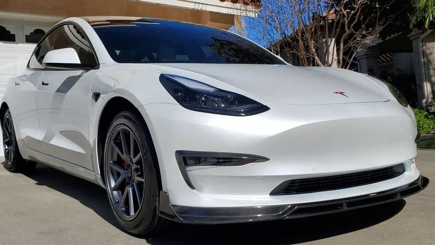 A white tesla model 3 is parked in front of a house.