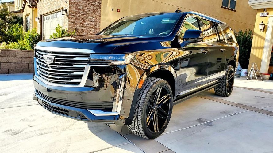 A black cadillac escalade is parked in a driveway in front of a house.