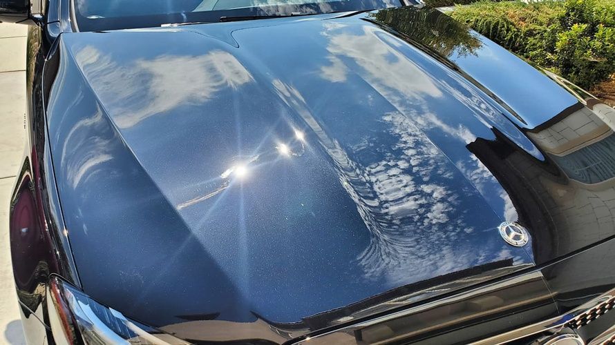 A black car with a shiny hood is parked on the side of the road.