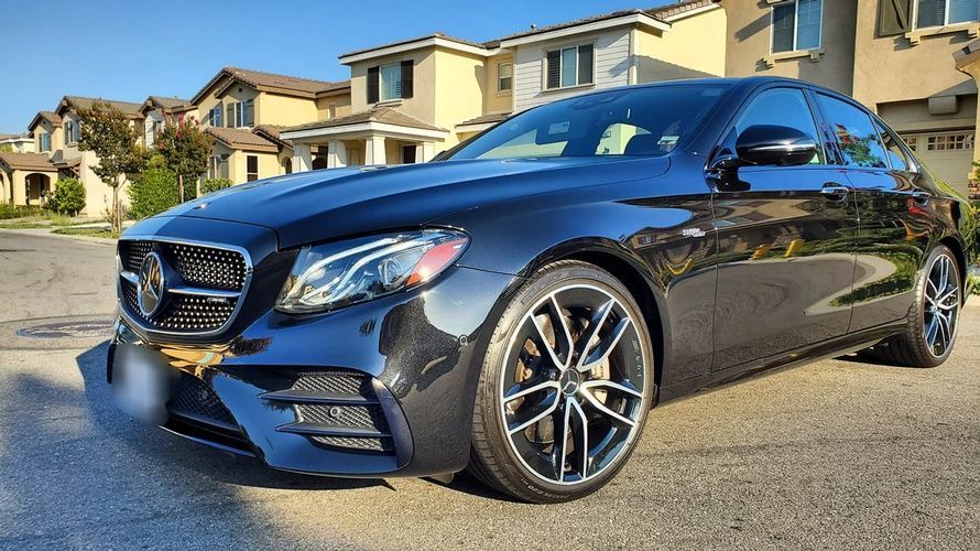 A black mercedes benz e class coupe is parked in front of a row of houses.