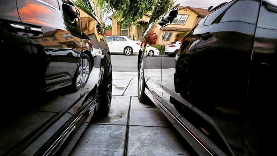Two black cars are parked next to each other on the side of the road.