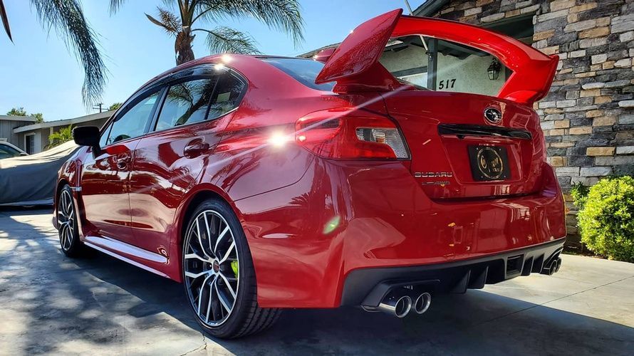 A red subaru wrx sti is parked in front of a stone building.