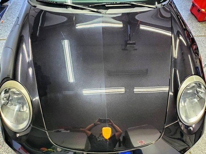 A black car is parked in a garage with the hood open
