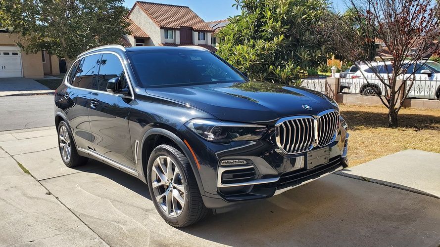 A black bmw x5 is parked in a driveway in front of a house.