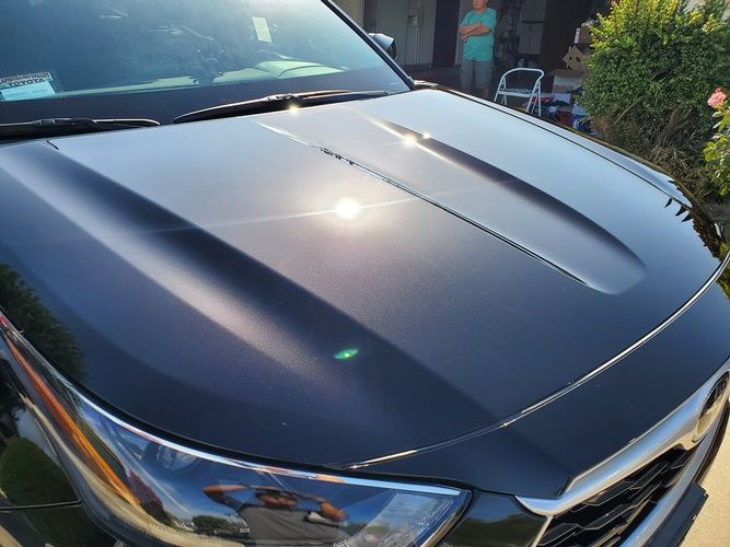 A black car with the hood up is parked in front of a house