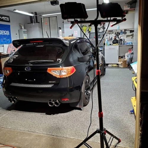 A black car is parked in a garage next to a light stand.