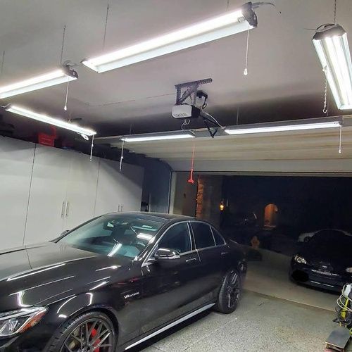 A black car is parked in a garage with a garage door open.