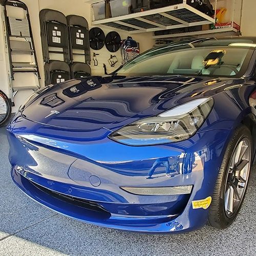 A blue tesla model 3 is parked in a garage.