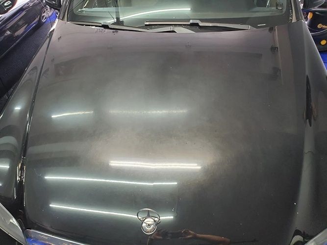 A black car is parked in a garage with the hood up.