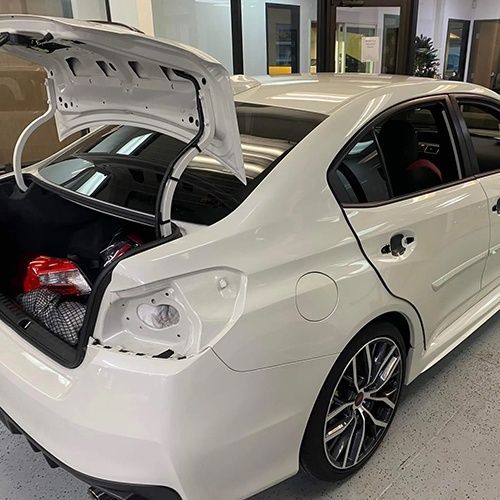 A white car with the trunk open is parked in a garage.