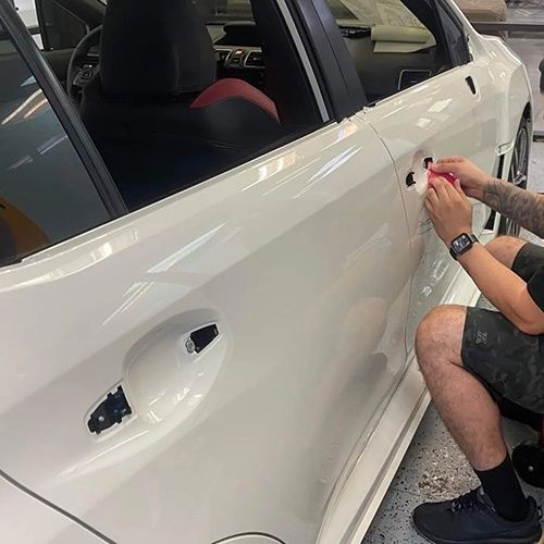 A man is kneeling down next to a white car.
