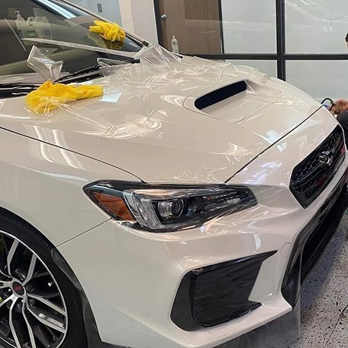 A man is wrapping a white car with plastic wrap.