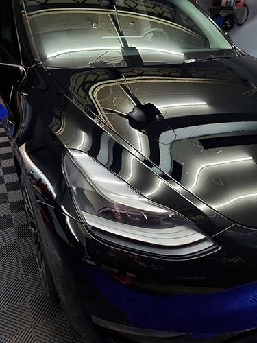 A black tesla model 3 is parked in a garage.