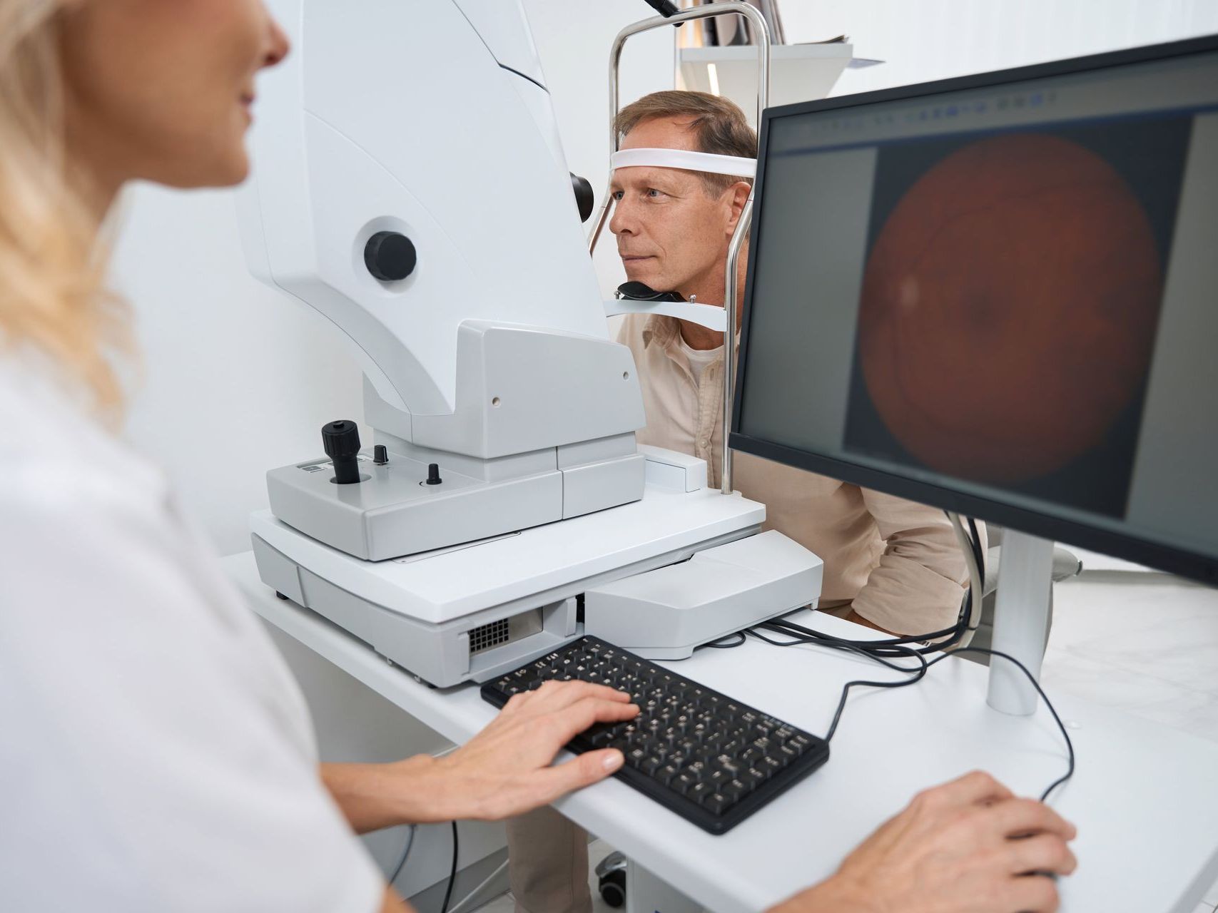 An image of a woman is using a computer to take a picture of a man's eye