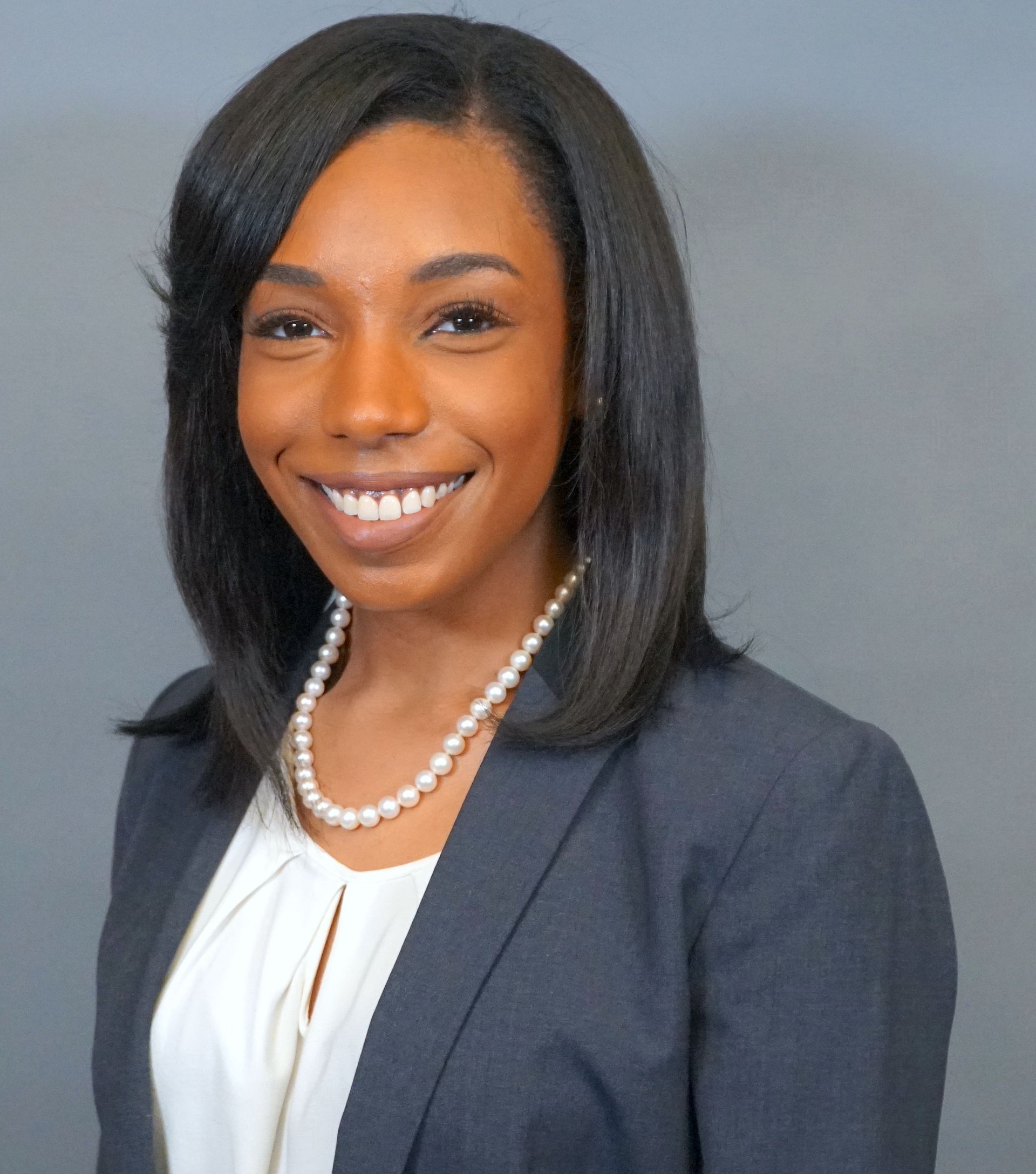 A woman wearing a pearl necklace and a suit jacket smiles for the camera