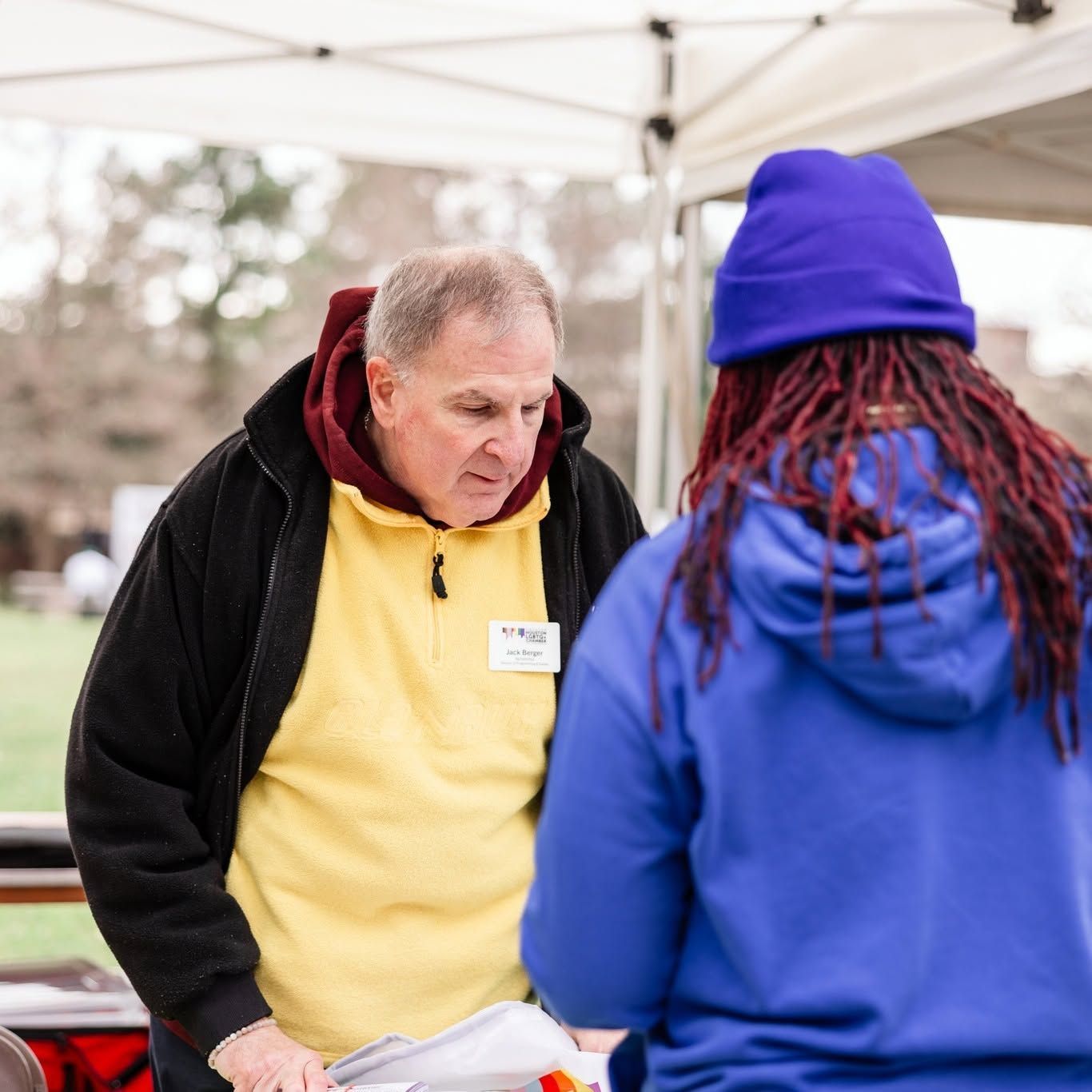 A male-presenting AIH volunteer standing at a booth, talking to a community member