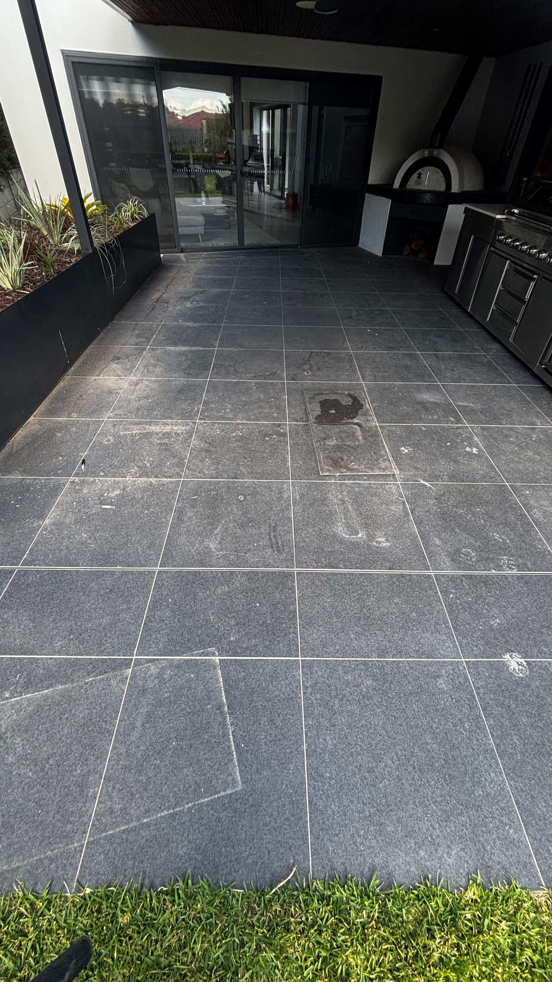 Outdoor tiled walkway leading to a building entrance, with black planters on the left and cabinets on the right.