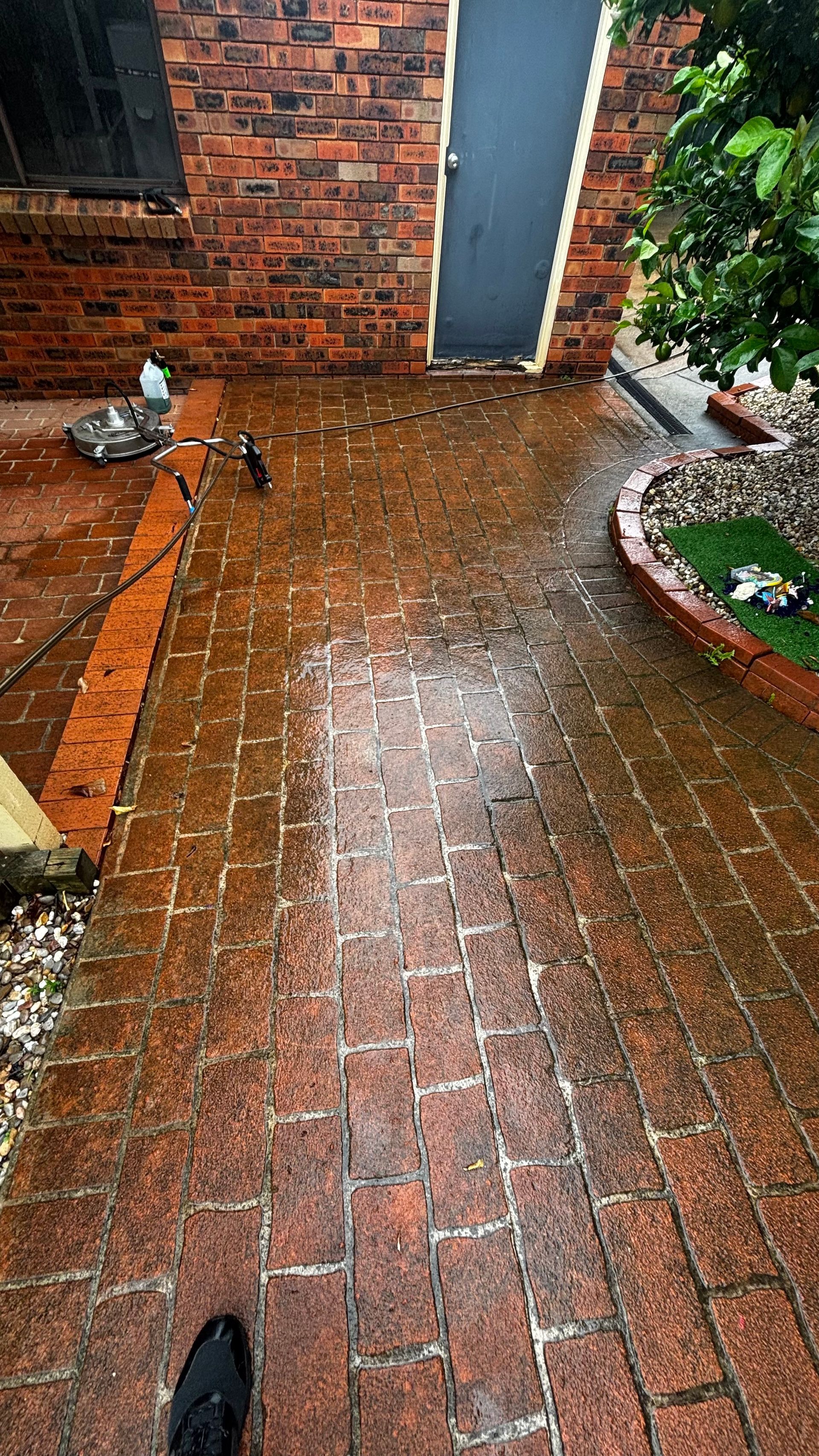 Rain-soaked brick patio beside a brick wall and garden bed, with a doorway at the end.
